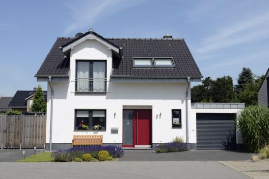 White two-story house features a black roof and a black garage door. A wood porch seat sits in front of the home's two large front windows. The entrance door is red. A wood privacy fence is featured on the left.