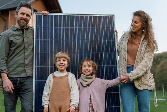 Die Kosten für eine Solaranlage sind nicht wenig. Trotzdem ist es vielen Familien wichtig, selbst Ökostrom zu produzieren. Familie mit Solarmodul vor ihrem Haus.