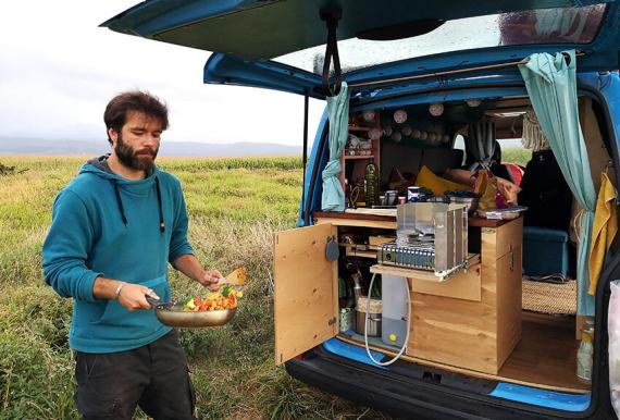 Felix steht mit einer Pfanne voll Gemüse an der Küche im Camper