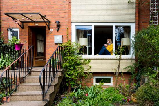 Vermögen mit 30: Frau sitzt im Fenster eines Reihenhauses