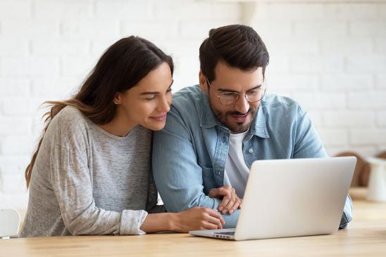 Paar sitzend am Tisch vor dem Laptop