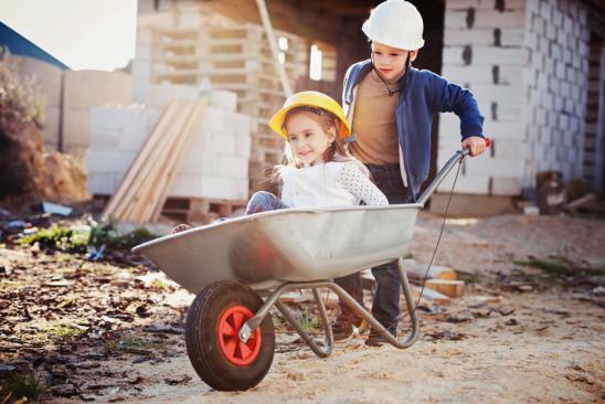 Zwei Kinder spielen mit einer Schubkarre auf einer Baustelle