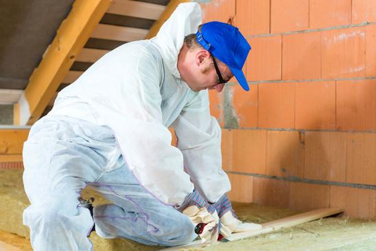 Dachboden durch Fachmann dämmen lassen. Handwerker schneidet Material, um Dachboden zu dämmen.