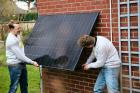 Zwei Männer installieren ein Balkonkraftwerk-Solarmodul an einer Hauswand