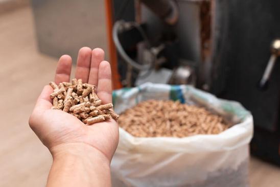 Ausgestreckte Hand mit Pellets vor geöffnetem Sack mit Pellets am Boden