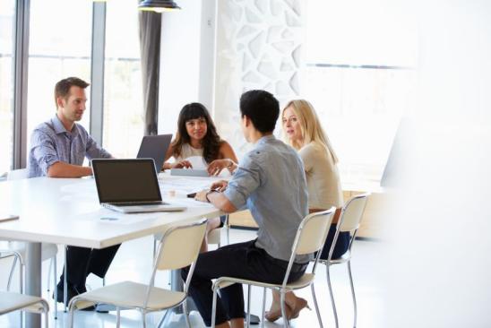 Vier Menschen sitzen an einem Tisch mit Laptops