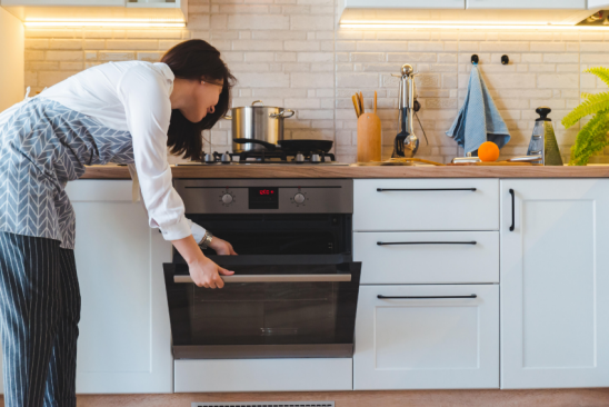 Junge Frau öffnet Backofen in der Küche