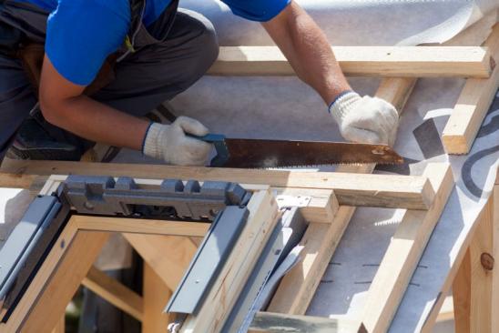 Skylight installation. Roofer builder worker use saw to cut a wooden beam