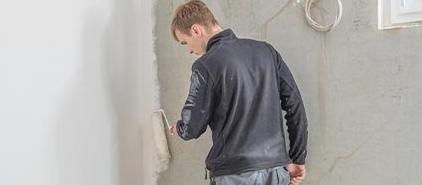 Handwerker beim Auftragen einer Dichtungsschicht an Kellerwand